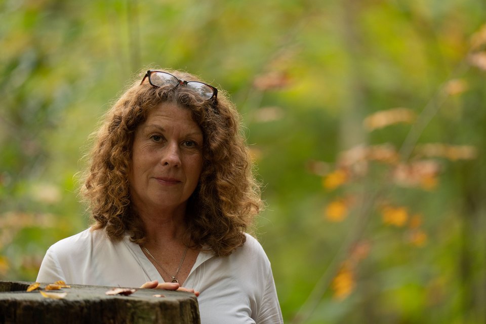 Michaela Molzahn im Wald, die Hand auf einem alten Holzpfosten.